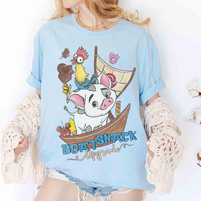 May include: Light blue t-shirt featuring a cartoon pig in a wooden boat with a sail. A rooster and various treats are also in the boat. The text "BOAT SNACK Upgrade" is printed below the boat in blue and gold.