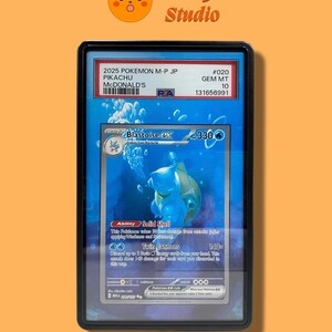 Puede incluir: Una carta coleccionable Blastoise ex certificada por PSA en una funda protectora negra. La carta presenta una ilustración azul con temática acuática, 330 HP y los ataques Solid Shell y Twin Cannons. La etiqueta dice 2025 POKEMON M-P JP PIKACHU MCDONALD'S #020 GEM MT 10.