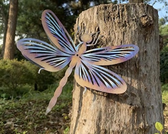 Pode incluir: Uma escultura de libélula de metal com asas iridescentes em tons de roxo, azul e dourado é montada em um tronco de árvore. A libélula tem padrões de asas detalhados e um corpo esguio, adequada para decoração de jardim ao ar livre.