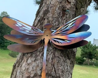 Pode incluir: Uma escultura de libélula de metal com asas iridescentes em tons de bronze, azul e roxo é montada em um tronco de árvore. A libélula tem um corpo e asas detalhados com padrões recortados, criando um elemento decorativo de jardim.