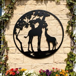 Puede incluir: Obra de arte de metal negro con silueta de jirafas. La obra presenta una jirafa y su cría bajo un árbol, dentro de un marco circular. Montada en una pared de ladrillo claro, con una jardinera de madera con flores coloridas debajo.