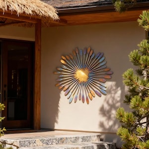 May include: A large, metallic sunburst wall sculpture. The central disc is gold, with radiating elements in shades of blue, purple, and bronze. It's mounted on a beige exterior wall, near a doorway and stone steps, creating a striking visual.