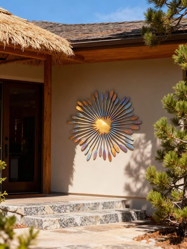 May include: A large, metallic sunburst wall sculpture. The central disc is gold, with radiating elements in shades of blue, purple, and bronze. It's mounted on a beige exterior wall, near a doorway and stone steps, creating a striking visual.