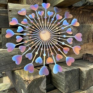 May include: A metal wall decoration with a circular design. It features heart-shaped elements that change colour from orange to blue. The artwork is mounted on a background of weathered wooden beams.