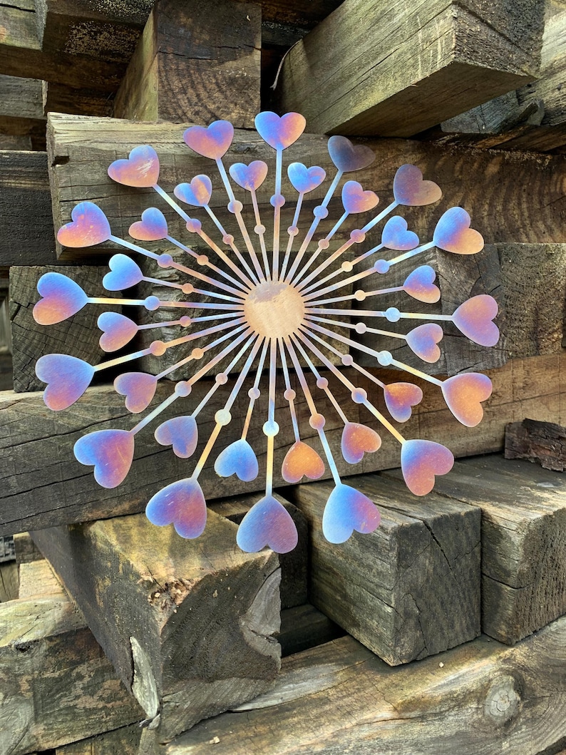 May include: A metal wall decoration with a circular design. It features heart-shaped elements that change colour from orange to blue. The artwork is mounted on a background of weathered wooden beams.