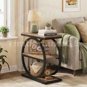May include: A side table with a black circular metal frame and two rectangular wooden shelves. The top shelf holds a beige lamp, a small potted succulent, and three stacked books. The bottom shelf contains a woven basket and a brass compass.