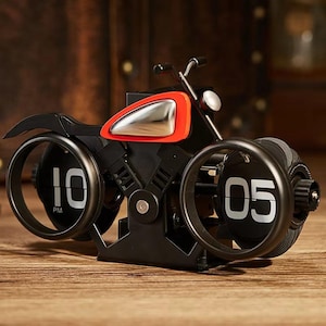 May include: A black and red motorcycle-shaped flip clock. The clock displays the time as 10 PM and 05. The clock has a silver fuel tank and a headlight. The clock is on a wooden surface.