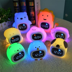 Puede incluir: Colección de coloridos despertadores digitales con forma de animales. Cada reloj muestra la hora y presenta un diseño único, como un oso, un león, un búho y un perro. Los relojes están iluminados con colores suaves y brillantes, creando un diseño lúdico.