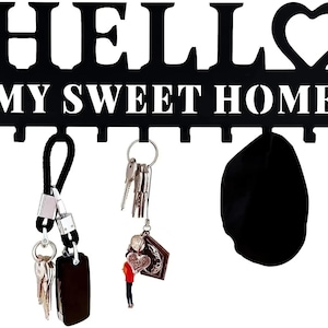 Puede incluir: Llavero de metal negro con las palabras "HELLO MY SWEET HOME" recortadas. El llavero tiene un diseño en forma de corazón y varios ganchos. Llaves y una bolsa negra cuelgan de los ganchos.