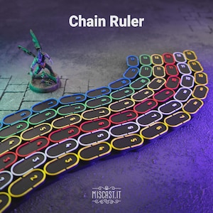 Op de afbeelding: Een Chain Ruler spelaccessoire bestaande uit een reeks verbonden, ovale schakels in zwart met kleurrijke randen en witte cijfers. De schakels zijn in een gebogen pad gerangschikt, naast een kleine, beschilderde gevleugelde miniatuur.