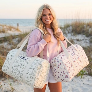 May include: Two floral-patterned duffel bags with cream-colored straps and the name "LILY" embroidered on them. One bag has a white background with a green floral print, and the other has a white background with a red and purple floral print.