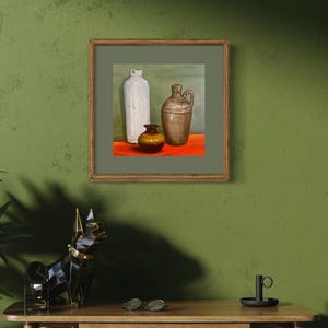 May include: A room interior featuring a wooden desk, a woven stool, and a framed painting of vases. A decorative dog statue and a potted plant in a bronze-coloured pot enhance the decor. The wall is painted a muted green.