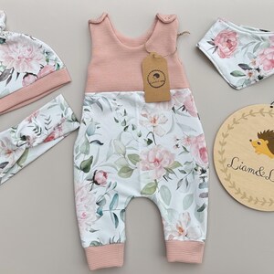 May include: A baby clothing set featuring a pink and white floral print. The set includes a romper, hat, headband, and bib. A wooden sign with a hedgehog illustration and the text "Liam & Luppy" is also included.