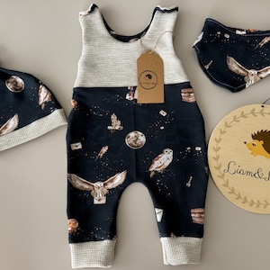 Puede incluir: Un conjunto de ropa para bebé con un estampado de búhos y lunas en azul marino. El conjunto incluye un pelele, un gorro y un babero. También se incluye un letrero de madera con una ilustración de erizo y el texto "Liam & Luppy".