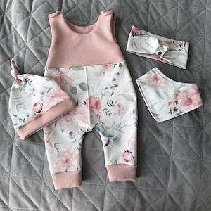 May include: A baby clothing set featuring a pink and white floral print. The set includes a sleeveless romper, a knotted hat, a headband, and a bib. The romper has a pink waffle-knit top and floral print bottoms.