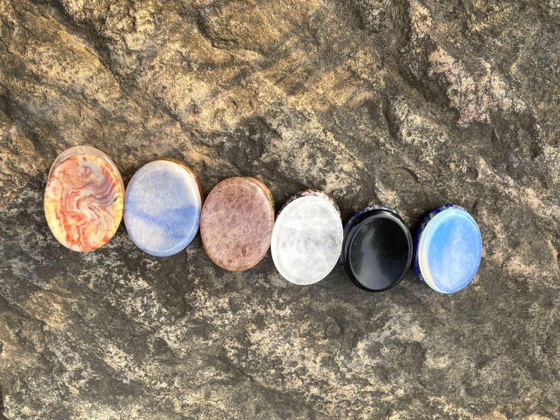 Puede incluir: Una colecci&oacute;n de siete piedras ovaladas en varios colores y patrones. Las piedras incluyen tonos de rojo, azul, marr&oacute;n, blanco y negro, con una &uacute;ltima piedra en azul y blanco. Las piedras est&aacute;n dispuestas en fila.