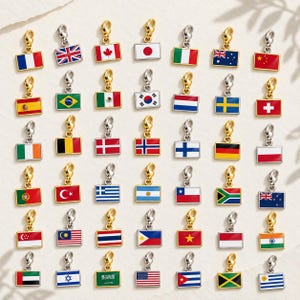 May include: A collection of rectangular metal flag charms, each featuring a small lobster clasp at the top. The charms display various national flags in vibrant enamel colors, including France, the UK, Canada, Japan, Italy, Australia, and China.
