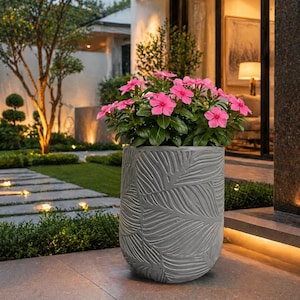 Puede incluir: Una maceta gris texturizada llena de vibrantes flores rosas. La maceta tiene un diseño de hojas y está colocada en un patio de piedra. La escena es al aire libre, con un césped bien cuidado y una casa al fondo.