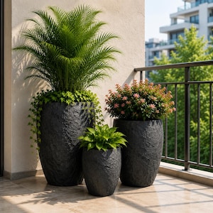 May include: Three dark gray, textured, oval-shaped planters of varying heights. The tallest planter holds a large green palm-like plant with trailing ivy. The medium planter contains a shrub with small pink flowers. The smallest holds green foliage.