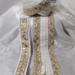 Peut inclure: Ensemble turban et écharpe assortie de couleur crème, orné de broderies dorées et argentées complexes. Le turban présente un motif en éventail plissé. L'écharpe comporte des glands décoratifs en bas. Coiffe traditionnelle pour occasions spéciales.