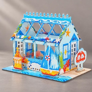 May include: A decorative miniature house model covered in colourful faceted beads. The structure features a blue roof with wave patterns, a sailboat cutout, a lighthouse, and coral reef motifs. The design includes starfish and sea-themed elements.