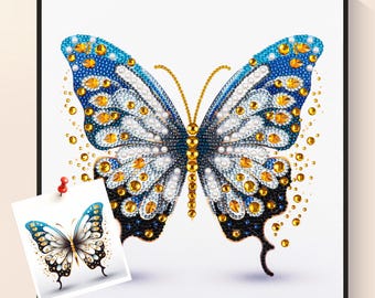 Puede incluir: Una obra de arte de mariposa enmarcada con un diseño detallado. La mariposa presenta alas azules, blancas y negras adornadas con adornos dorados y perlados. Una imagen más pequeña de la mariposa está sujeta al marco.