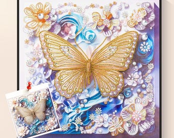 Puede incluir: Obra de arte enmarcada que presenta una gran mariposa dorada con detalles intrincados, rodeada de adornos florales blancos, azules y morados. Incluye una imagen de muestra más pequeña del diseño de la mariposa.