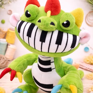 May include: A plush green monster toy with a piano key mouth, red horns, and colorful claws. The toy has large, round eyes and a friendly expression. The toy is approximately 12 inches tall.