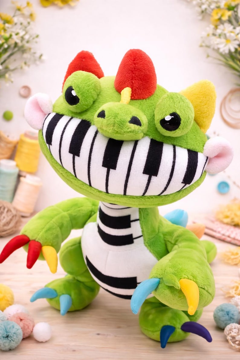 May include: A plush green monster toy with a piano key mouth, red horns, and colourful claws. The toy has large, round eyes and a friendly expression. The toy is approximately 30 cm tall.