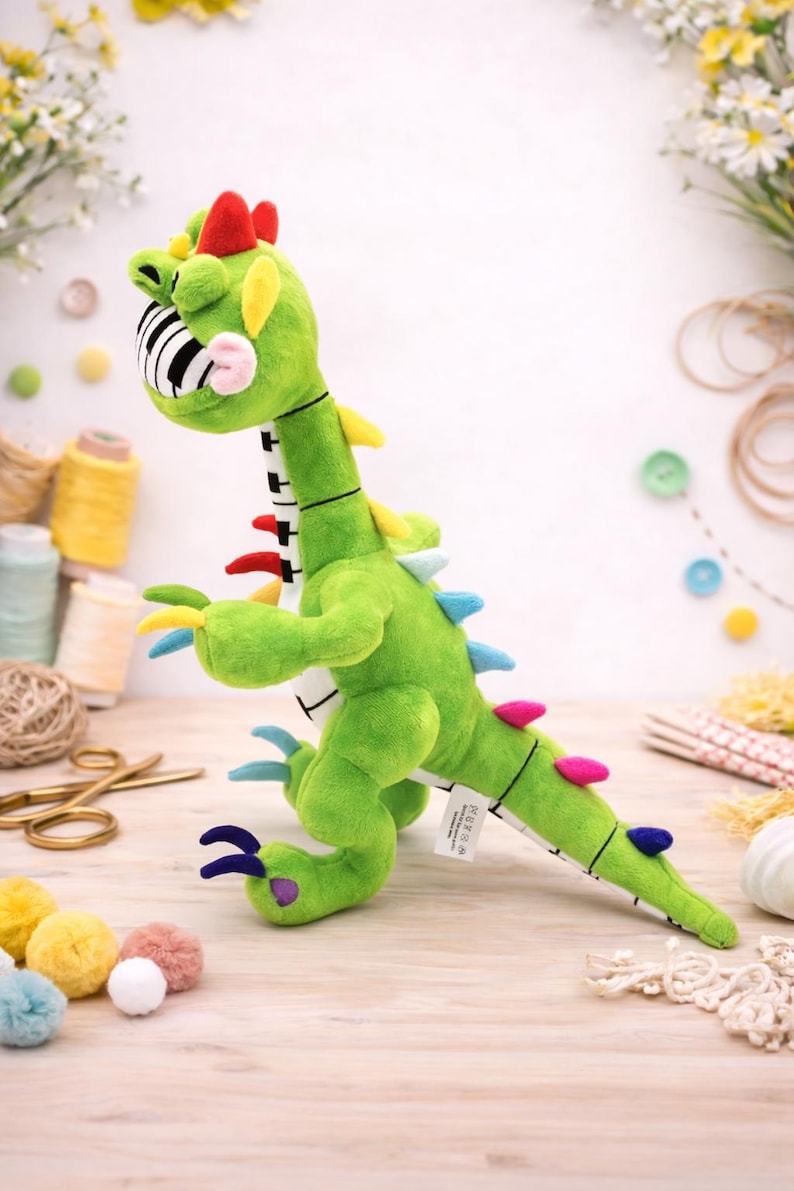 May include: A green plush dinosaur toy with a piano key-patterned mouth and colourful accents. The toy has red, yellow, blue, and pink details, and is designed to resemble a musical instrument. It is a whimsical and playful item.