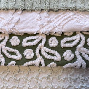 May include: A stack of four textured fabric pieces in shades of green and white. The top piece is a light green with vertical ridges. Below it is a white piece with a floral design. The third piece is olive green with white leaf patterns.