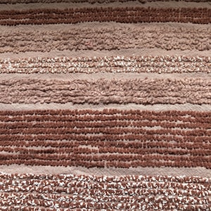 May include: A close-up of a textured fabric with horizontal stripes in shades of brown and pink.