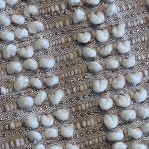 May include: Close-up of a textured fabric with a woven pattern. The fabric has a light brown background with white raised dots.