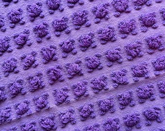 May include: Purple fabric with a repeating pattern of small, raised, textured circles.