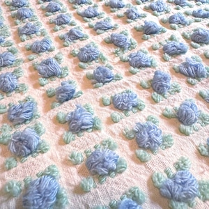May include: A white crocheted throw blanket with a repeating pattern of blue and green flowers.