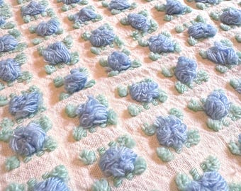 Puede incluir: Una manta de crochet blanca con un patrón repetitivo de flores azules y verdes.
