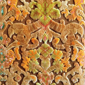 May include: Close-up of a brown fabric with a raised, embossed pattern of flowers and leaves in shades of orange, yellow, and green.