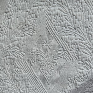 May include: White quilted fabric with a raised, embossed pattern of stylized leaves and flowers.