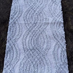 Op de afbeelding: Een lichtgrijze badmat met een getextureerd, gelust ontwerp. Het patroon heeft onderling verbonden ovale vormen, waardoor een zacht, pluche uiterlijk ontstaat. De mat is rechthoekig en lijkt gemaakt van absorberend materiaal.