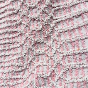 May include: Close-up of a textured fabric with a pattern of pink and white stripes. The fabric has a soft, plush appearance, with a raised, looped texture. The design creates a visual rhythm.
