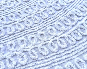 Puede incluir: Primer plano de una tela blanca texturizada con un patrón repetitivo de bucles y líneas. La tela parece suave y afelpada, con un diseño en bucle en relieve. El fondo es de un color claro y neutro.