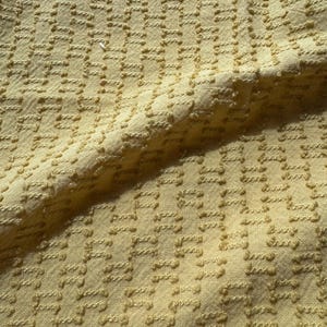 May include: A close-up of a yellow textured fabric with a woven pattern. The fabric has a subtle sheen and a soft, slightly bumpy texture.