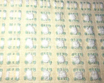 Puede incluir: Una tela amarilla con un patrón tejido verde y blanco. La tela tiene una superficie texturizada con pequeños bultos blancos.