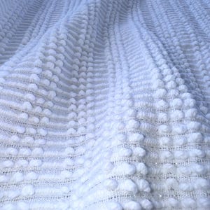 Peut inclure: Tissu blanc texturé avec un motif de points en relief. Le tissu est tissé et a un léger brillant.