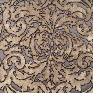 May include: Close-up of a fabric with a repeating damask pattern. The design features gold-colored, ornate floral and scrollwork against a gray background. The pattern is outlined in a darker, almost black color.