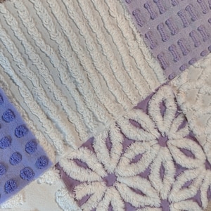 May include: A white and purple patchwork quilt with a variety of textures. The quilt is made of different fabrics with different patterns, including a floral pattern, a striped pattern, and a polka dot pattern.