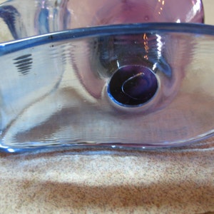 May include: A blue and purple glass bowl with a unique, wavy design. The bowl has a hole in the center.