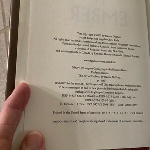 Puede incluir: P&aacute;gina abierta de un libro con texto de copyright de 2003 de Jeanne DuPrau. El texto describe el libro "The City of Ember" e incluye el ISBN y los datos de la Biblioteca del Congreso. Es una primera edici&oacute;n impresa en Estados Unidos.