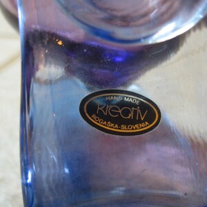 May include: A blue glass vase with a label that reads "Hand Made Kreativ Rogaska-Slovenia".