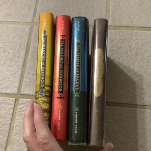 Puede incluir: Cuatro libros de tapa dura con lomos coloridos son sostenidos por una mano. Los libros se titulan "The Diamond of Darkhold", "The Prophet of Yonwood", "The People of Sparks" y "The City of Ember". Los libros son publicados por Random House.